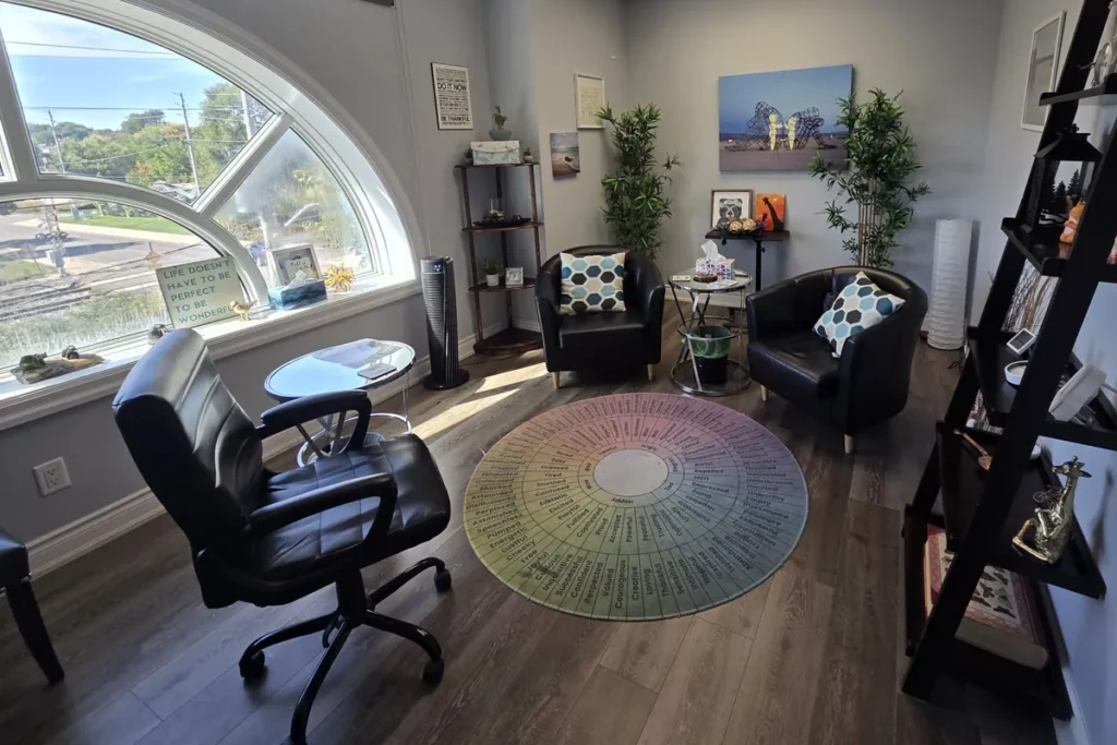 Bright therapy room with an arched window, two black armchairs and an emotion-wheel rug at the Mississauga office