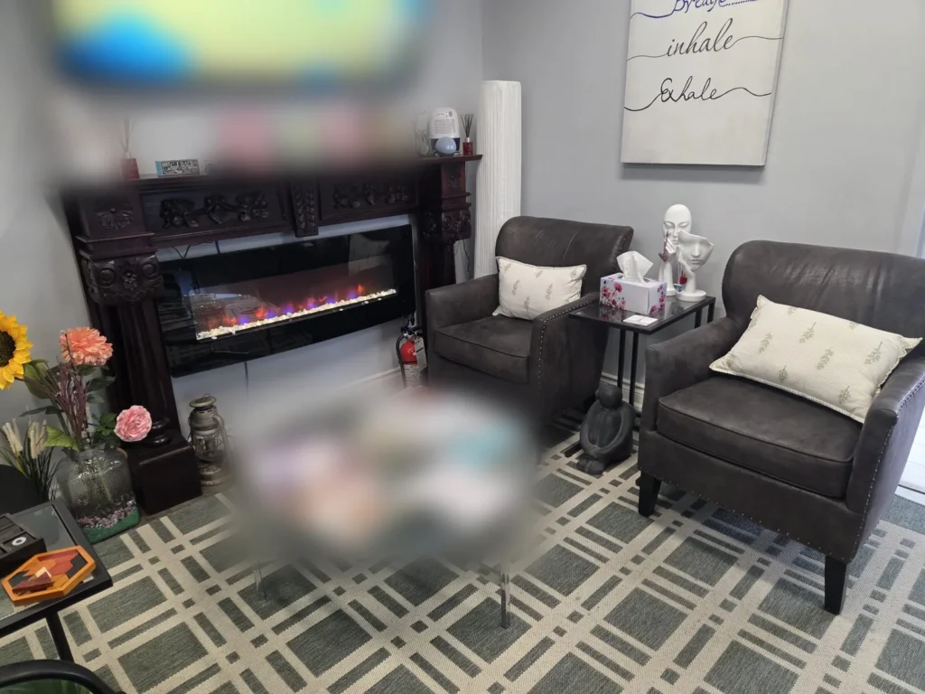 Waiting area at Serenity Psychotherapy Clinic in Mississauga, with two armchairs, a glass coffee table and an electric fireplace.